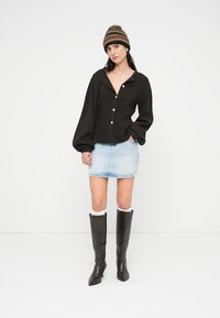 Μαύρο πλεκτό πουκάμισο με κουμπιά και βαθύ γιακά, ανοιχτό μπλε μίνι φούστα από τζιν και καφέ σκούρα μπότες με τακούνι μέχρι το γόνατο. Συνοδεύεται από ριγέ σκουφί.