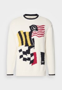 Pull en maille de couleur crème avec des motifs de drapeau multicolores, incluant rouge, bleu, jaune et noir. Doté d'un col et de manchettes en côte bleu marine.