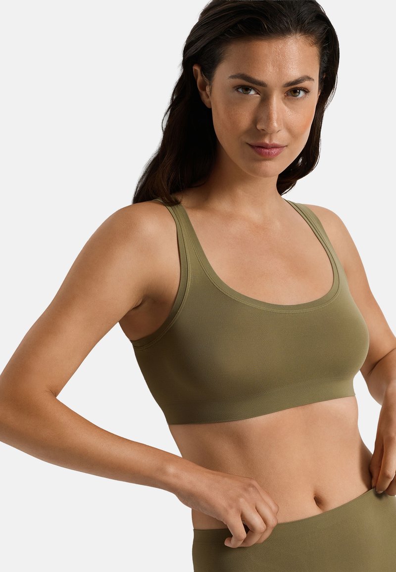 Femme portant un soutien-gorge de sport sans coutures vert olive et un bas taille haute assorti, sur un fond clair uni.