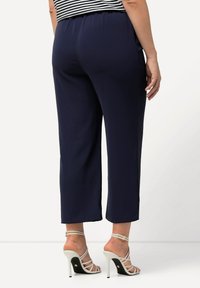 Námořnické zkrácené kalhoty s elastickým pasem, které mají hladkou texturu. Vydáno s bílými sandály na vysokém podpatku se řemínky.