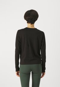 Svart långärmad tröja i ett slätt tyg med rund halsringning. Bakdelen har en figursydd design, kombinerad med gröna leggings.