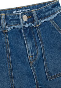 Jeans de mezclilla azules de talle alto con cinturilla deshilachada, cierre de botón de metal y detalle de costura naranja visible.