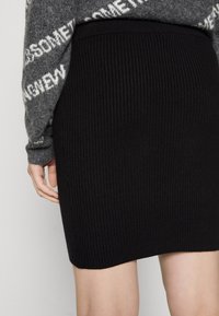 Svart ribbad stickad kjol med en figurnära form, som har ett brett midjeband, en slät textur och en knälång nederkant.