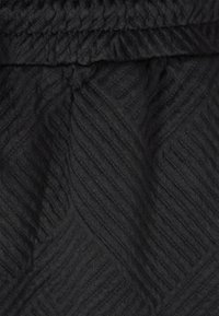 Svart texturerad tyg med ett diagonalt ribbmönster och elastiskt midjeband, med en slät och något glansig yta.