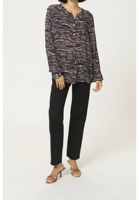 Blusa a maniche lunghe blu navy con un motivo astratto texturizzato in arancione e bianco, chiusura con bottoni sul davanti, pantaloni neri slim-fit. Sandali con tacco marroni.