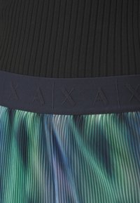 Gros plan d'une jupe plissée avec un motif bleu-vert multicolore et une ceinture bleu marine embossée des lettres "AX".