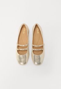 Goldene metallische Mary Jane-Schuhe mit runden Zehen, doppelten Riemen und Schnallen sowie glatter Textur. Das Clarks-Logo ist auf der Innensohle sichtbar.