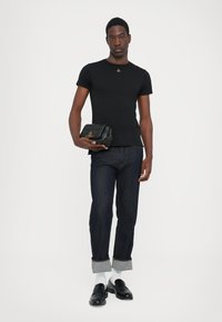 Tricou negru cu mânecă scurtă, având un logo mic, purtat cu blugi închis la culoare, șosete albe și mocasini negri. Ținând în mână o geantă clutch neagră, cu model matlasat.
