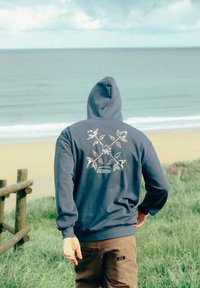 Hoodie bleu marine avec un grand motif floral au dos, présentant des pétales colorés et une fleur centrale, fabriqué en matière douce.