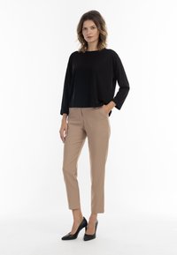 Maglietta nera a maniche lunghe e pantaloni beige su misura. L'outfit presenta una vestibilità comoda con una texture morbida e scarpe con tacco alto nere.