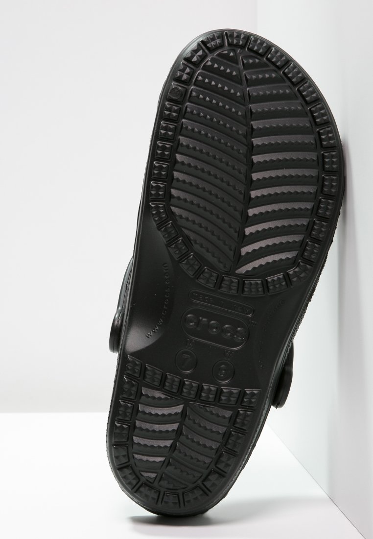 Suela de zapato de goma negra con patrones de agarre texturizados, que presenta triángulos elevados y ranuras para tracción. Incluye marcas de talla en la base.