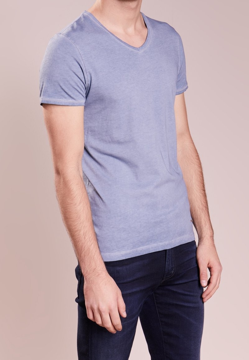 T-shirt bleu clair à col en V en tissu doux, design ajusté, manches courtes et détail de couture subtil. Assorti à un jean foncé.