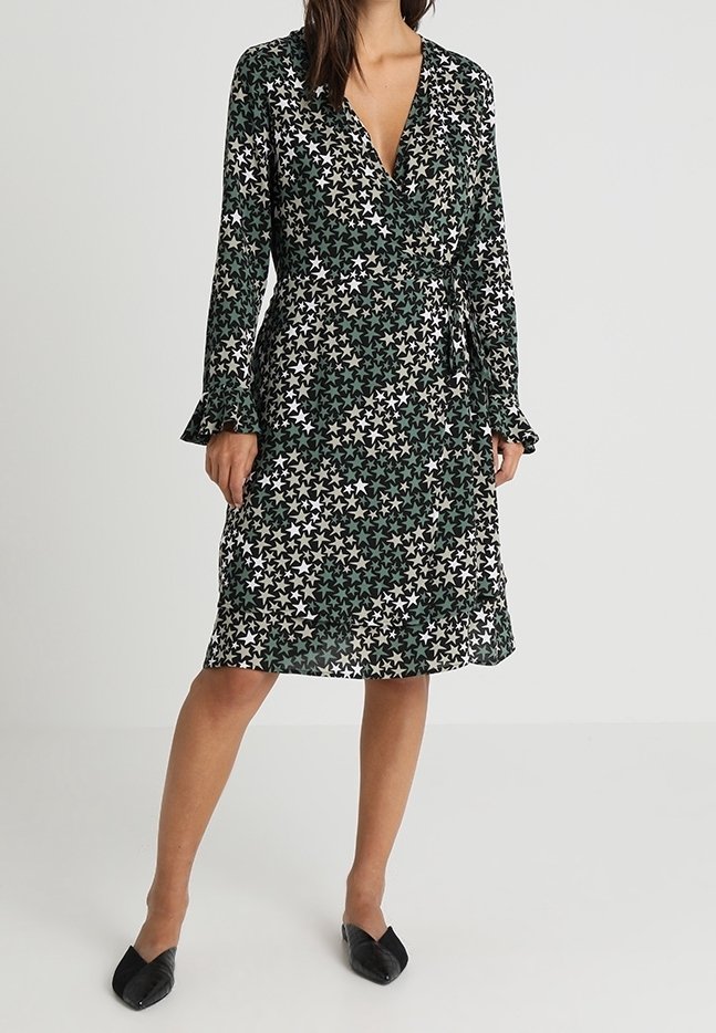 Schwarzes Wickelkleid mit grünem und weißem Sternenmuster, langen Ärmeln und ausgestellten Manschetten. Leichter Stoff, knielang mit tailliertem Bund.