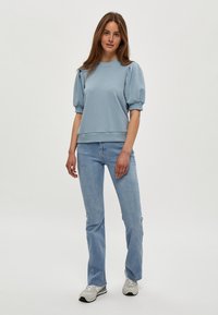 Ljusblå sweatshirt med puffärmar, ribbad nederkant, kombinerad med ljusblå jeans och grå sneakers. Enkel, avslappnad design.