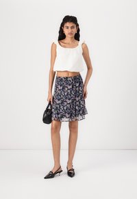 Haut court blanc à volants avec un décolleté carré. Jupe midi fleurie avec un fond noir et des fleurs colorées. Petit sac à main noir et talons aiguilles.