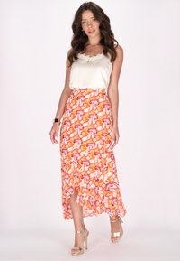 Maxi rok met een multicultureel abstract patroon in roze, oranje en wit; gecombineerd met een crèmekleurige satijnen top en metallic hakken.