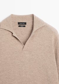 Maglione beige in 100% lana con collo a costine e scollo a V. Texture morbida, stile minimalista senza motivi o accenti visibili.