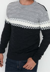 Pull en maille avec un motif texturé composé de rayures horizontales grises, blanches et noires. Poignets et ourlet côtelés. Motif décoratif de feuilles blanches.