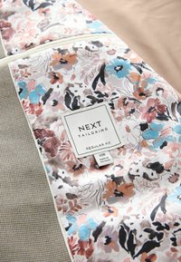 Intérieur d'une veste à motif floral avec une étiquette en tissu indiquant "NEXT Tailoring Regular Fit" et une étiquette de taille "40R Fabriqué au Vietnam".