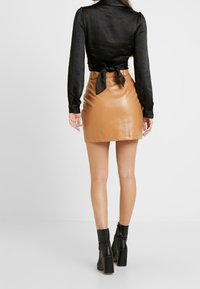 Mustat pitkät hihat blouse, jossa on sidottu selkä, sekä vaalea tekonahkainen mini-hame. Mustat nilkkurit, joissa on paksut korot, täydentävät asua.