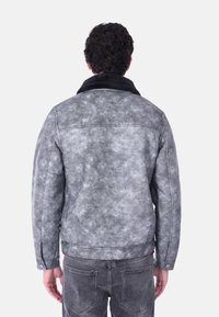 Giacca grigia con texture e colletto in pelliccia sintetica nera. Presenta un design uniforme, dettagli con bottoni e una vestibilità leggermente aderente.