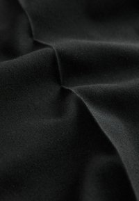 Schwarzer Stoff mit glatter Textur, der ein leicht zerknittertes Muster zeigt. Das Material wirkt leicht und weich.