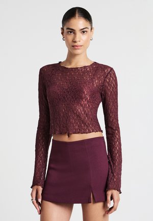 Top in pizzo bordeaux a maniche lunghe con orlo corto, caratterizzato da un motivo testurizzato, abbinato a una gonna mini coordinata con una spaccatura laterale.