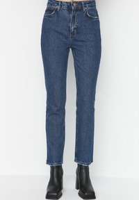 Jeans a vita alta blu in denim, con una linea dritta e una leggera scoloritura; indossati con stivaletti neri alla caviglia.
