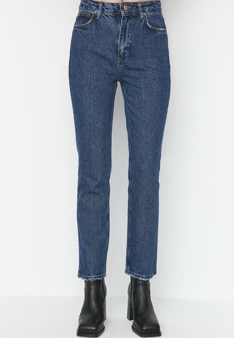 Jeans a vita alta blu in denim, con una linea dritta e una leggera scoloritura; indossati con stivaletti neri alla caviglia.