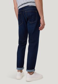 Donkerblauwe spijkerbroeken met opgerolde boorden, vijf zakken en contrasterende stiksels. Gecombineerd met witte sneakers.