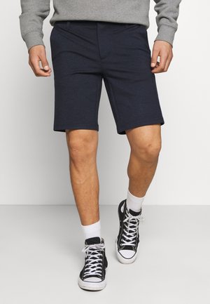 Marineblå shorts lavet af blødt stof, knælange, med sidelommer. Stylet med sorte høj-top sneakers og hvide sokker.