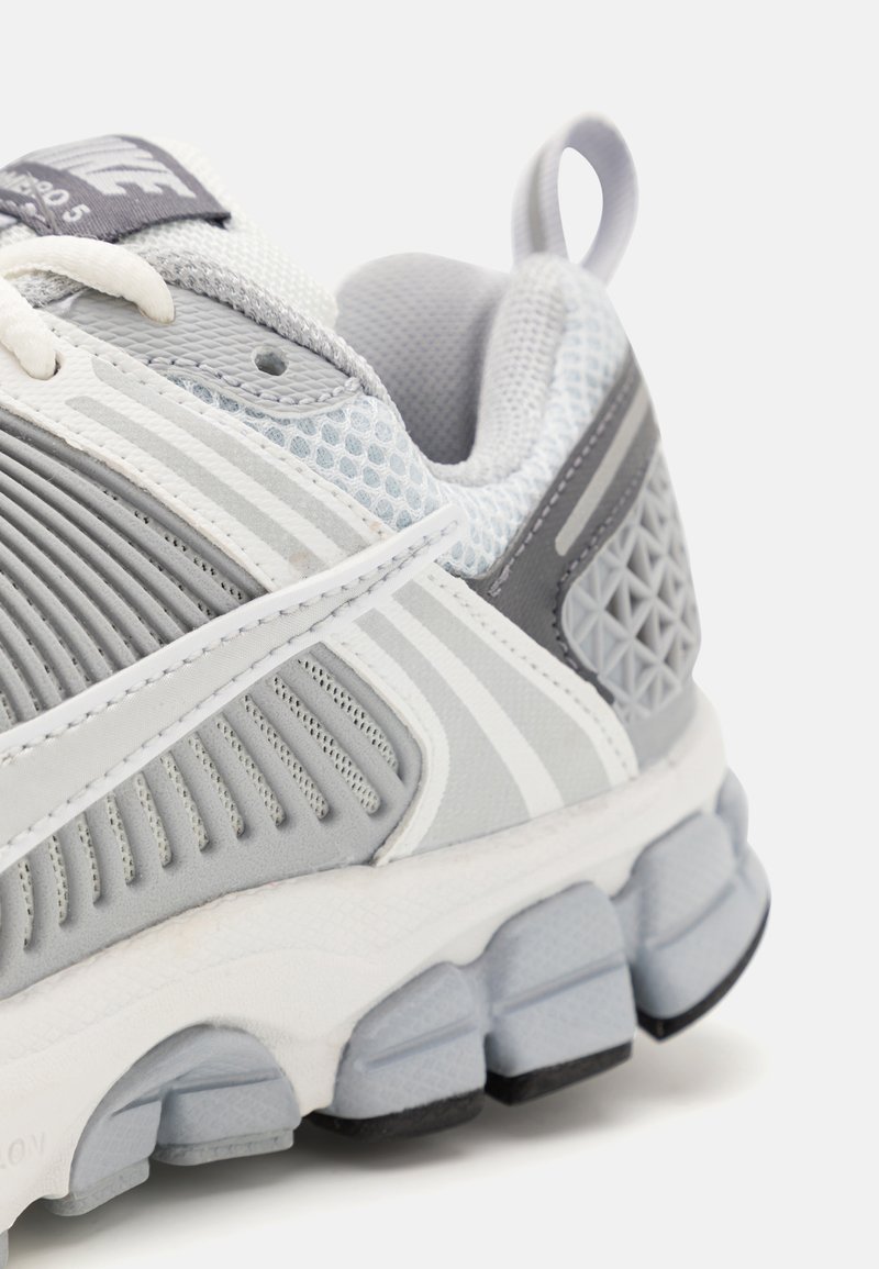 Grijze sport schoen met een bovenwerk van mesh en synthetisch materiaal, gestructureerde accenten, witte strepen en een gevoerde zool met gesegmenteerde pods.
