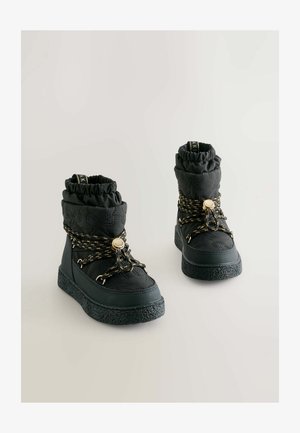 Crne kviltane gležnjače s teksturiranim gumennim potplatima, s pertlama s zlatnim akcentima i nabranim gornjim dijelom za udobno pristajanje.