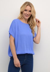 Top blu corto a maniche, realizzato in un tessuto morbido e testurizzato, con una vestibilità ampia, abbinato a jeans in denim scuri. Scollo rotondo semplice.