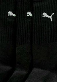 Three pairs of black ribbed socks with white Puma logo near the top, arranged vertically against a black background.