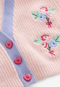 Soft pink knit fabric with light purple trim, decorated with red heart-shaped buttons and embroidered floral bouquets in red, blue, and green.