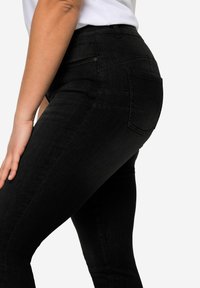 Vaqueros skinnies de mezclilla negra con cintura alta, que cuentan con bolsillos laterales, cierre de cremallera y detalles de costura en los bolsillos traseros.