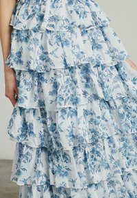Vestido de capas florales que presenta una tela en azul claro y blanco con volantes, adornado con varios patrones florales azules y una textura suave.