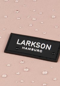 Vaaleanpunainen vedenpitävä kangas, jossa on koholla olevia pisaroita, mustassa suorakulmaisessa tarrassa lukee valkoisella tekstillä "LARKSON HAMBURG".