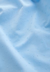 Hellblauer Stoff mit subtiler Textur, der kleine, erhabene Punktermuster gleichmäßig über die Oberfläche verteilt zeigt. Glattes, leichtes Material.