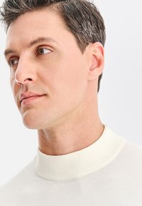 Biały prążkowany sweter z golfem o dopasowanym kroju. Gładka faktura, wysoki kołnierz, minimalistyczny design i subtelne detale przeszyć.