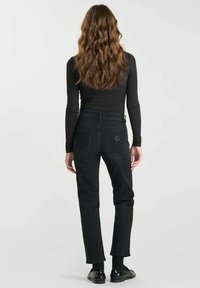 Jeans de mezclilla negra con corte recto, cinco bolsillos y un detalle de logo en la parte trasera, combinados con un top ajustado de manga larga.