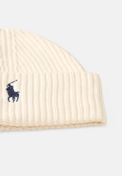 Gorro canelado em creme, feito de material suave, com uma dobra na bainha e um logótipo bordado em azul-marinho de um cavalo e cavaleiro.
