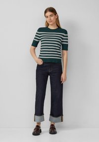 Grün gestreiftes Strickoberteil mit kurzen Ärmeln, kombiniert mit weitgeschnittenen Jeans aus dunklem Denim mit umgeschlagenen Säumen und braunen Lederloafers.