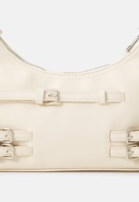 Cream-colored leather handbag with silver hardware, dual buckle accents, a rounded top, and a zip closure along the seam.