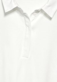 Vit polo skjorta med en texturerad tyg, klassisk krage och två knappar vid halsen. Designen är enkel och ren.