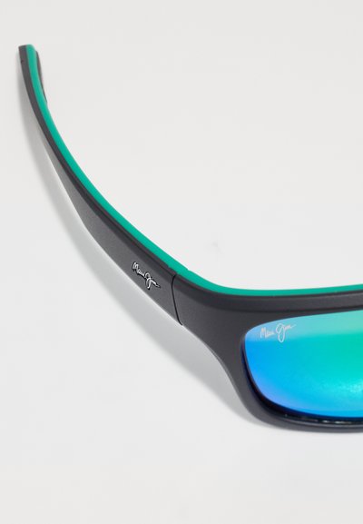 Mustat aurinkolasit, joissa on tyylikäs muotoilu, vihreä korostus yläreunassa ja peiligradianttilinssejä. Maui Jim -logo näkyvissä.