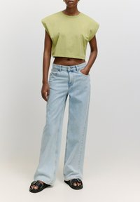 Lichtgroene cropped T-shirt met schouderaccenten, gecombineerd met lichtblauwe wijdvallende jeans. Zwarte sandalen met een gespsluiting.