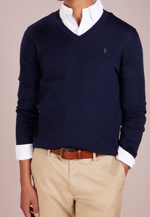 Navy v-neck sweater made of soft material, featuring long sleeves and a small logo. Paired with khaki pants and a brown belt. White collar visible.