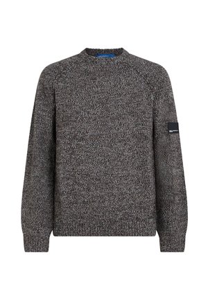 Pull tricoté gris et noir tacheté avec manches longues, col rond et petite étiquette noire rectangulaire avec logo sur le haut de la manche gauche.